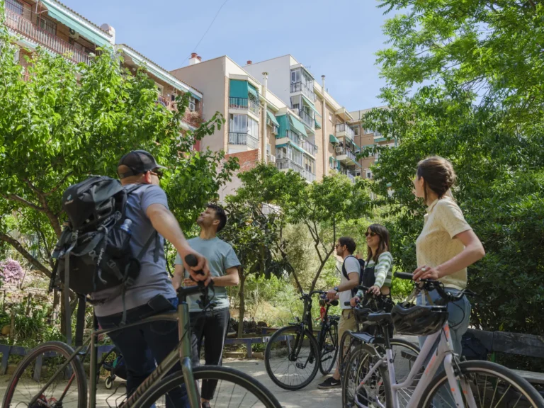 Hidden Madrid bike tour 2 Group of cyclists pause in a leafy Madrid plaza, looking up at typical balconied apartment buildings during the Hidden Madrid bike tour