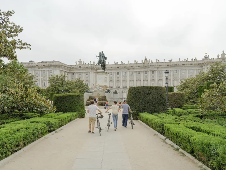Hidden Madrid bike tour 17 Travelers walk with their bikes through the formal gardens of Plaza de Oriente towards the Royal Palace of Madrid, a stop on the Hidden Madrid bike tour