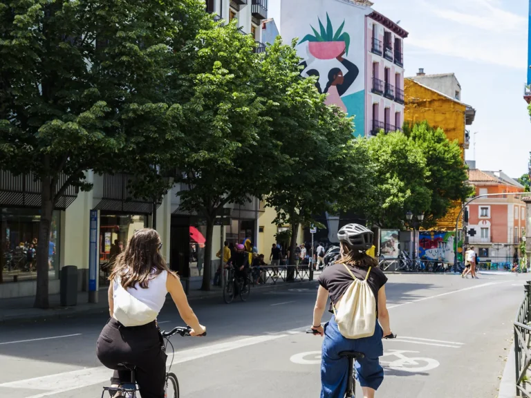 Private Madrid Bike Tour 6 Two cyclists ride a tree-lined bike lane past a colourful street mural on a private Madrid bike tour