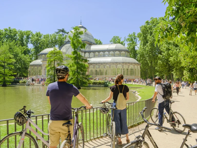 Private Madrid Bike Tour 2 Cyclists pause by the pond facing the Crystal Palace in Retiro Park on a private Madrid bike tour