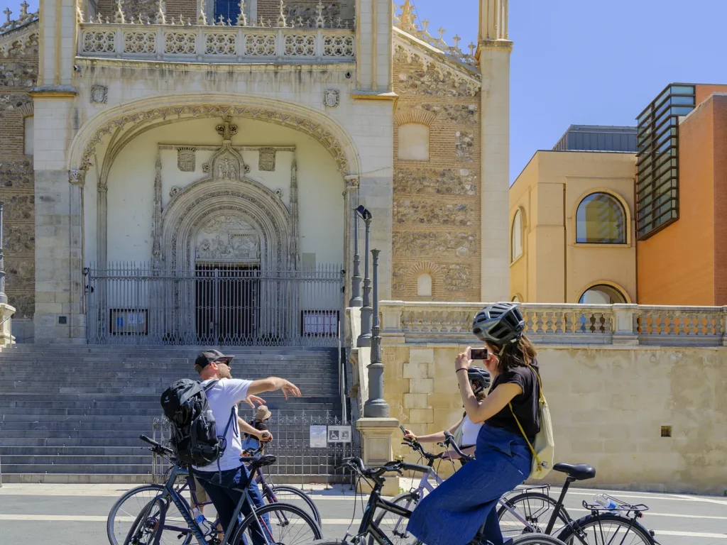 unusual things to do in Madrid 19 The guide points out the Gothic façade of Los Jerónimos beside the Prado while a rider photographs it, on bike tours, Madrid, Spain