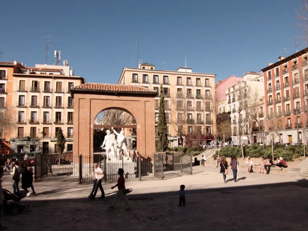 unusual things to do in Madrid 12 Locals cross the Dos de Mayo square in Malasaña in front of the brick arch and the Daoíz and Velarde statue, a stop on my Madrid tours