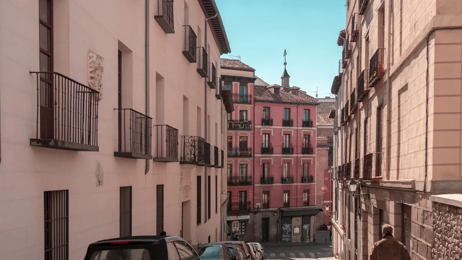 things to do in madrid by bike 3 A steep, narrow street in Lavapiés, Madrid, with wrought-iron balconies and a pink façade at the bottom